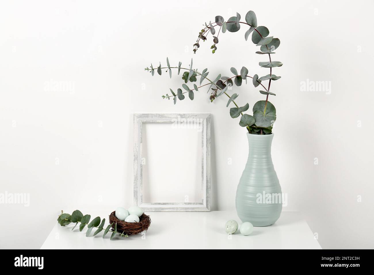 Blank frame, vase with eucalyptus branches and Easter eggs on white ...