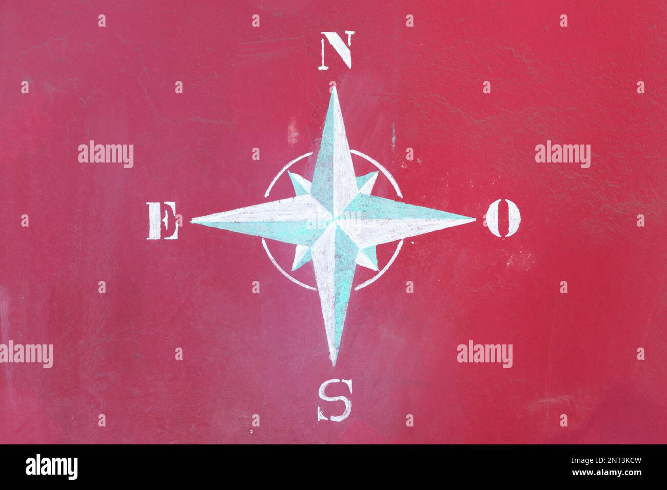 Close-up on an 8-point compass rose drawn with a chalk on a red wall. Stock Photo