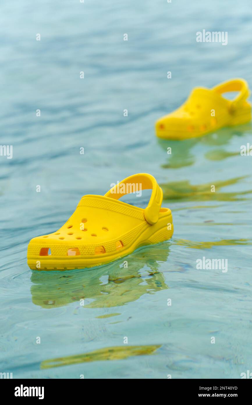 Lightweight pvh syellow slippers swimming on a water surface. Convenient footwear concept Stock Photo