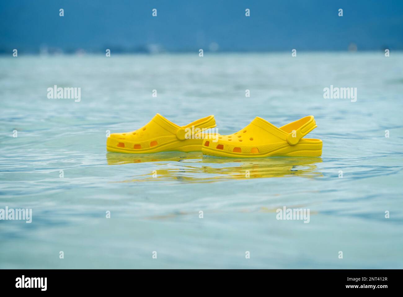 Lightweight pvh syellow slippers swimming on a water surface. Convenient footwear concept Stock Photo