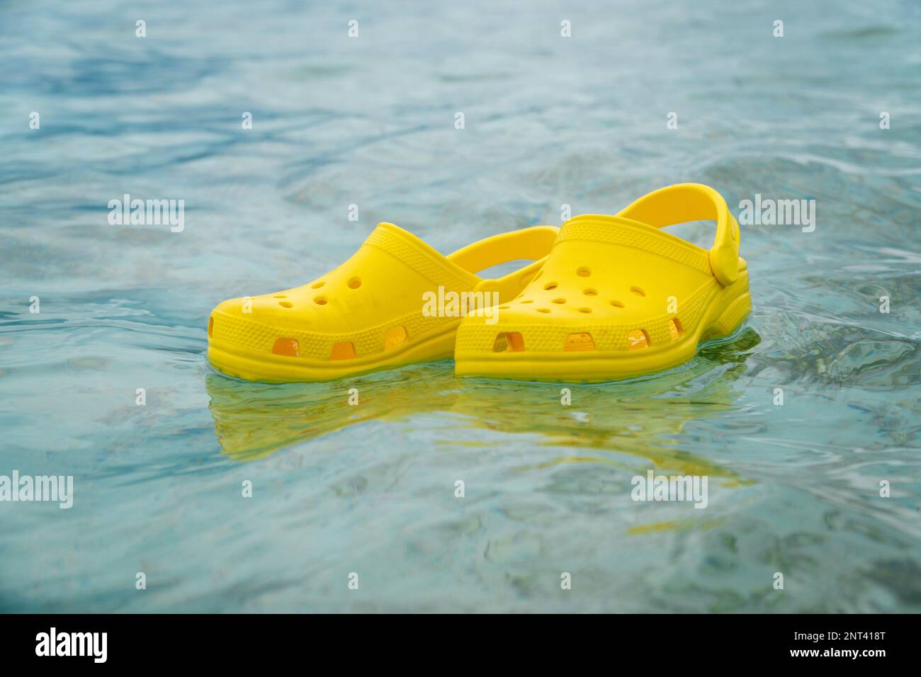 Lightweight pvh syellow slippers swimming on a water surface. Convenient footwear concept Stock Photo