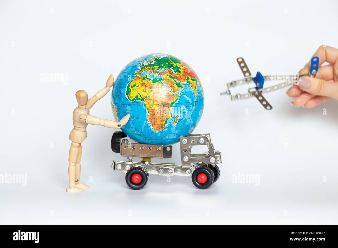 Globe on a children's cargo car and a wooden person with a back and a small plane in his hands on white, international trade Stock Photo