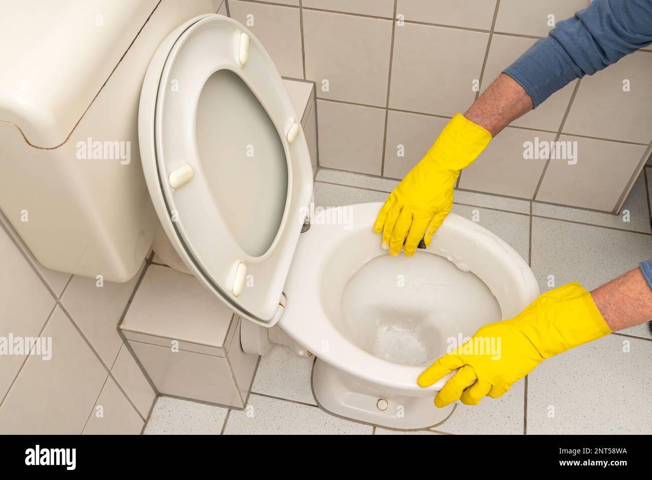 Hands of a man in yellow gloves cleaning the toilet bowl in the