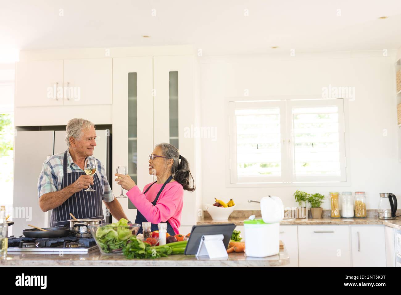 Happy senior diverse couple cooking dinner in kitchen, drinking wine Stock Photo