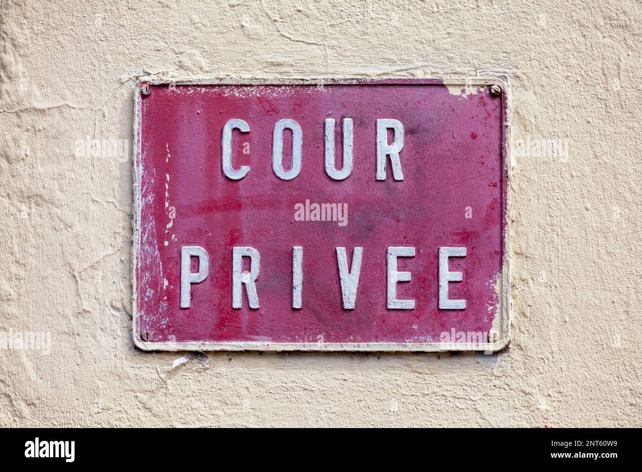 Metal plate painted in red a screwed on a wall painted in beige. The plate state in French “Cour privée”, meaning in English “Private courtyard”. Stock Photo