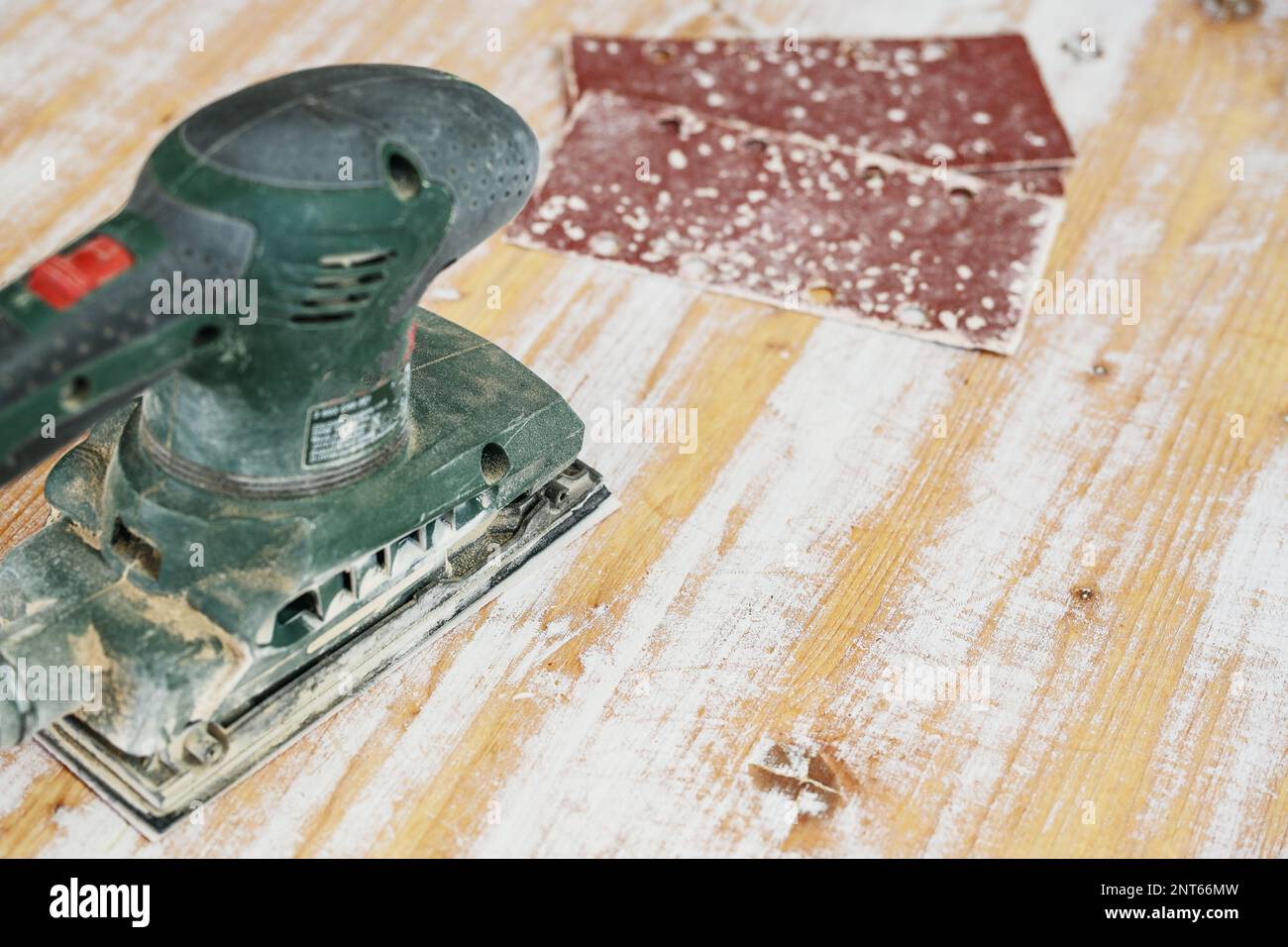Electric orbital sander removes layers of white paint from a wooden