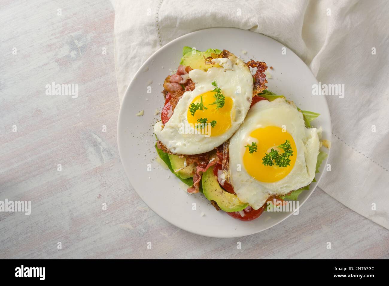Brunch sandwich with fried egg, avocado and bacon on a white plate and a light wooden table, high angle view from above, copy space, selected focus Stock Photo