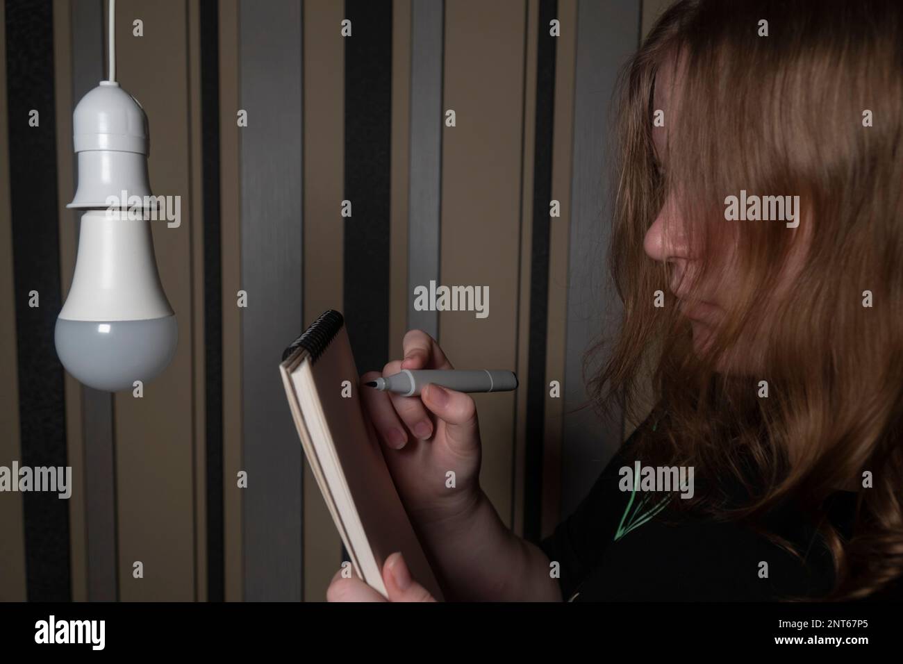 A girl with a notebook and a pen in a dark room looks at an electric