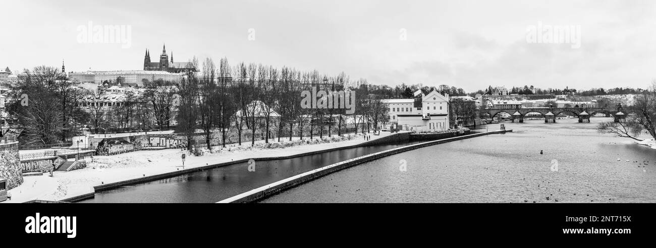 Panoramic view of Kampa Island during winter in Prague, Czech Republic. In the foreground, there is the Vltava riverbank with the Sova Mills, Czech: Sovovy Mlyny, complex. In the background, there is a view of Prague Castle and the Charles Bridge. Black and white photography. Stock Photo