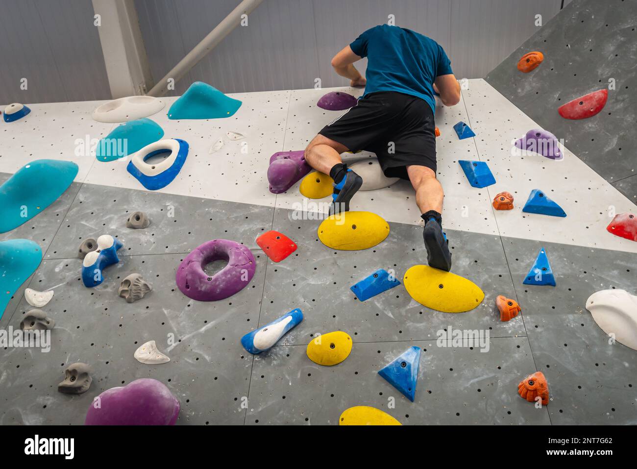 Man high up climbing indoor climbing wall using holds and grips of