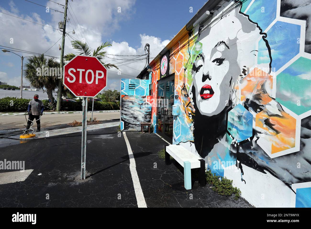 In this Thursday, June 20, 2019 photo, Antani (cq) Ray Walter pressure  washes the sidewalk next to a Marilyn Monroe mural on the side of Red Pear  Yoga at the Hive, a