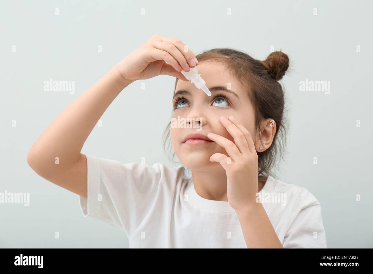 Adorable little girl using eye drops on white background Stock Photo