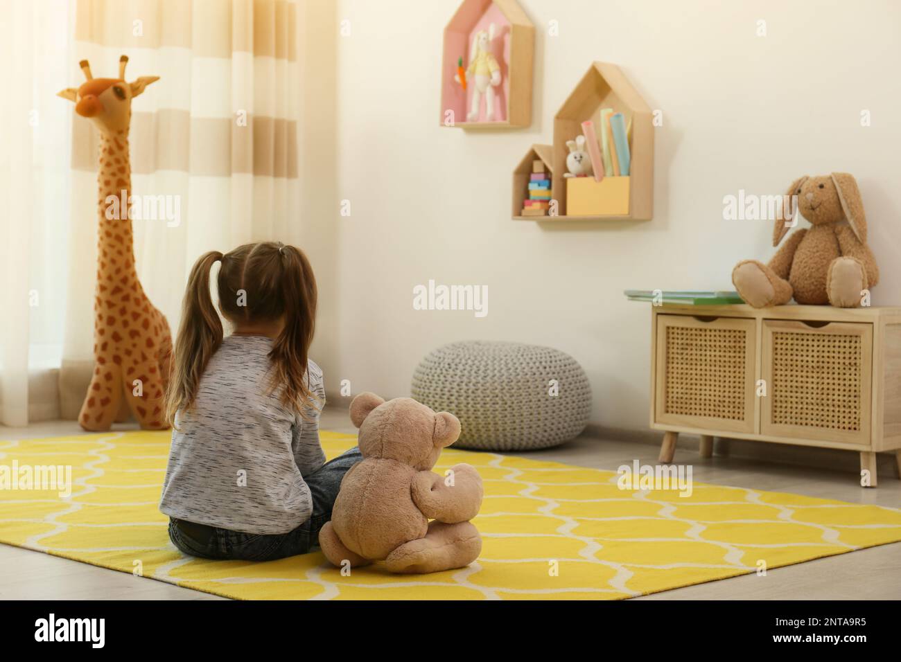 Lonely little girl with teddy bear sitting on floor at home, back view ...