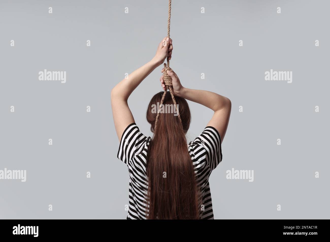 Woman with rope noose on neck against light grey background, back view