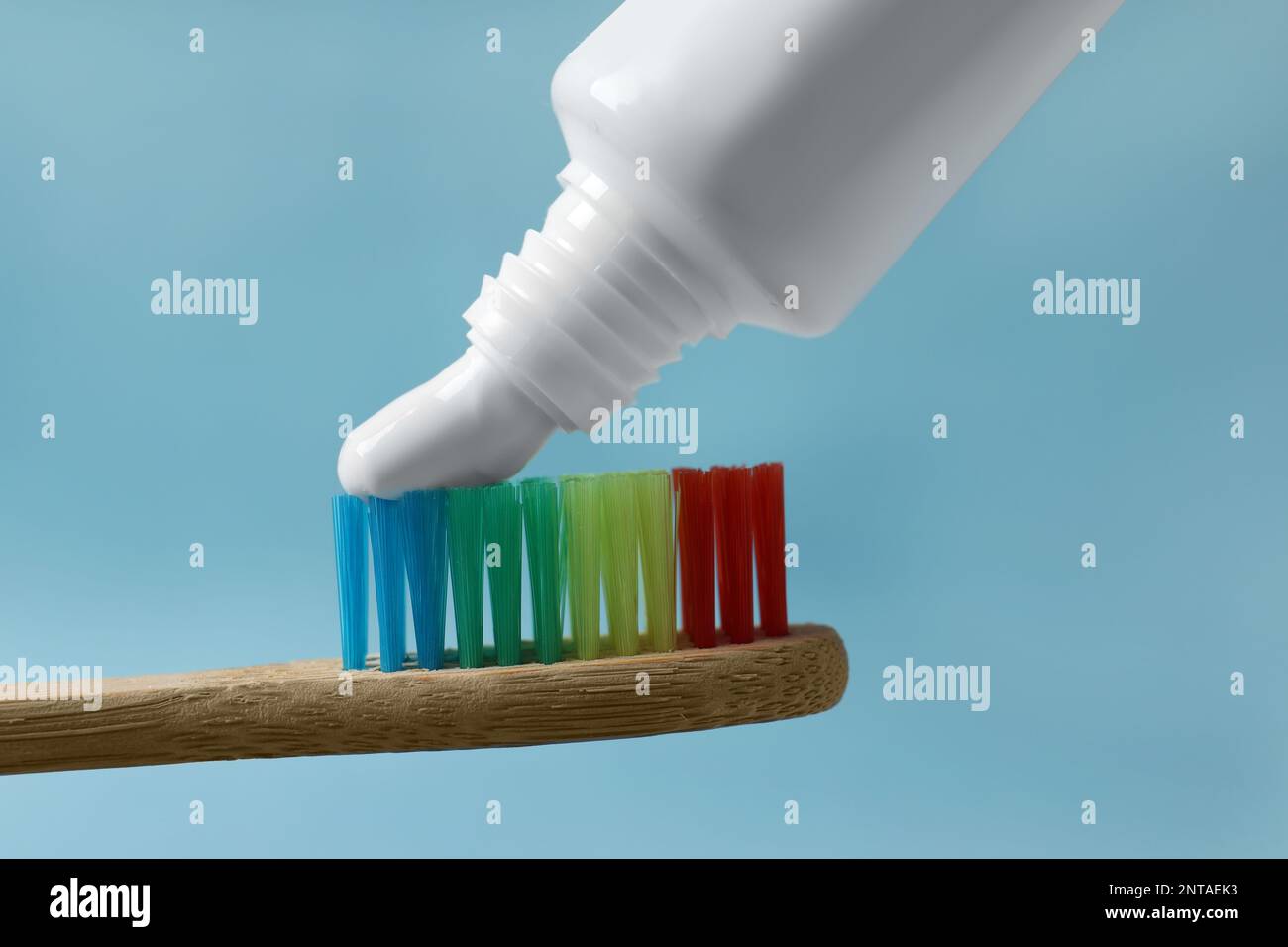Squeezing toothpaste onto brush against light blue background, closeup
