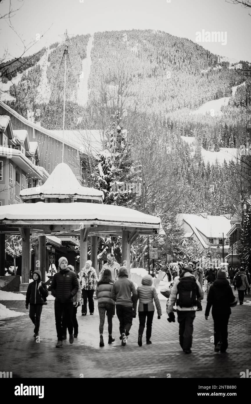 Black and white image of tourists walk through the Whistler Village on a snowy winter afternoon.  Whistler BC, Canada. Stock Photo