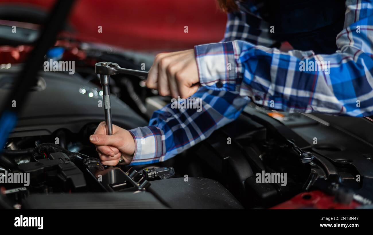 Female auto mechanic unscrewing a nut to replace a car spark plug Stock