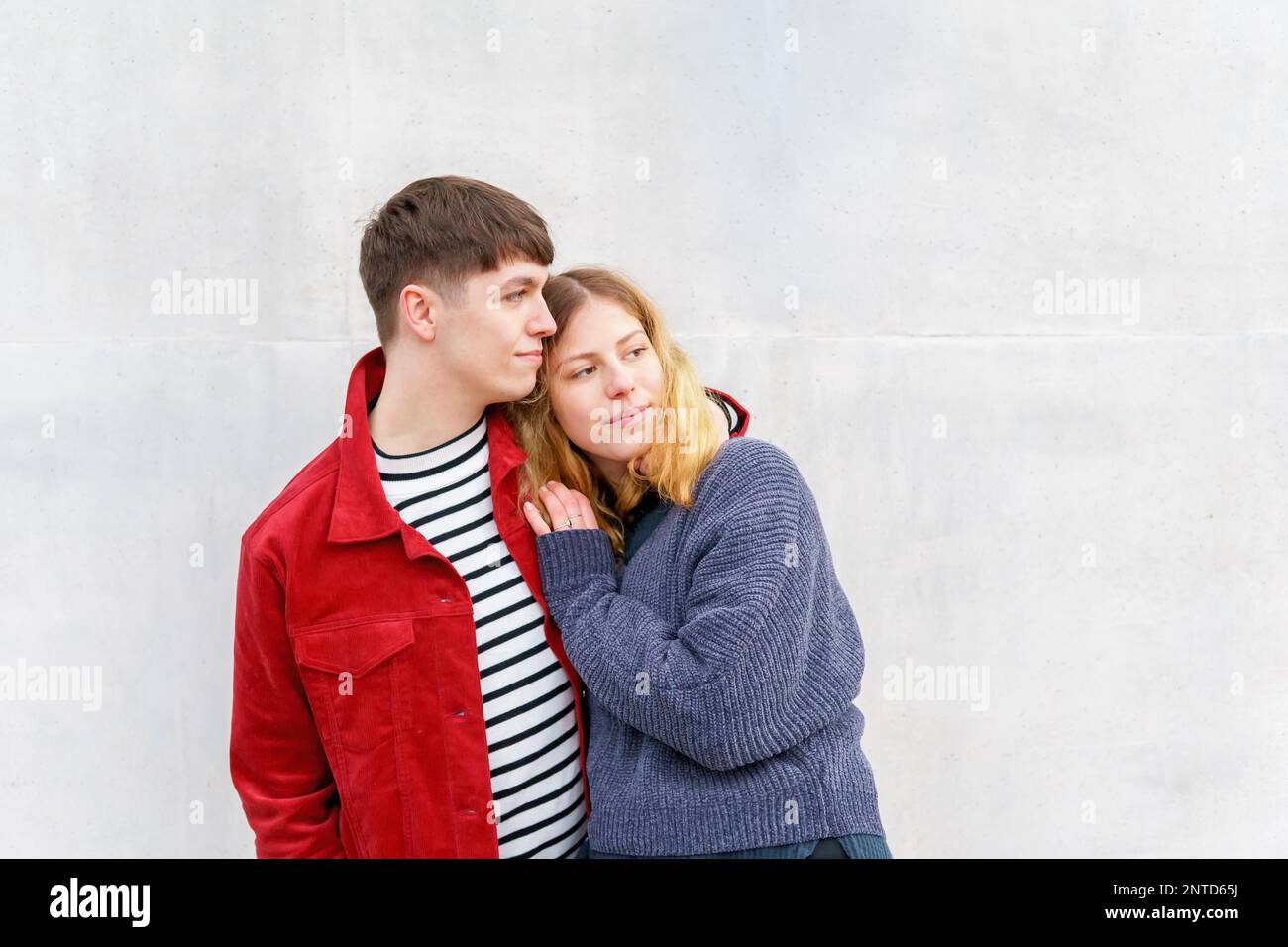 young affectionate couple standing in front of concrete cement wall loooking towards copy space Stock Photo