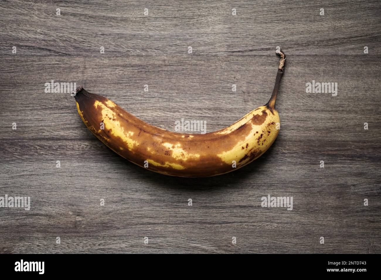 overhead view of overrripe banana fruit with brown skin on rustic wooden background Stock Photo