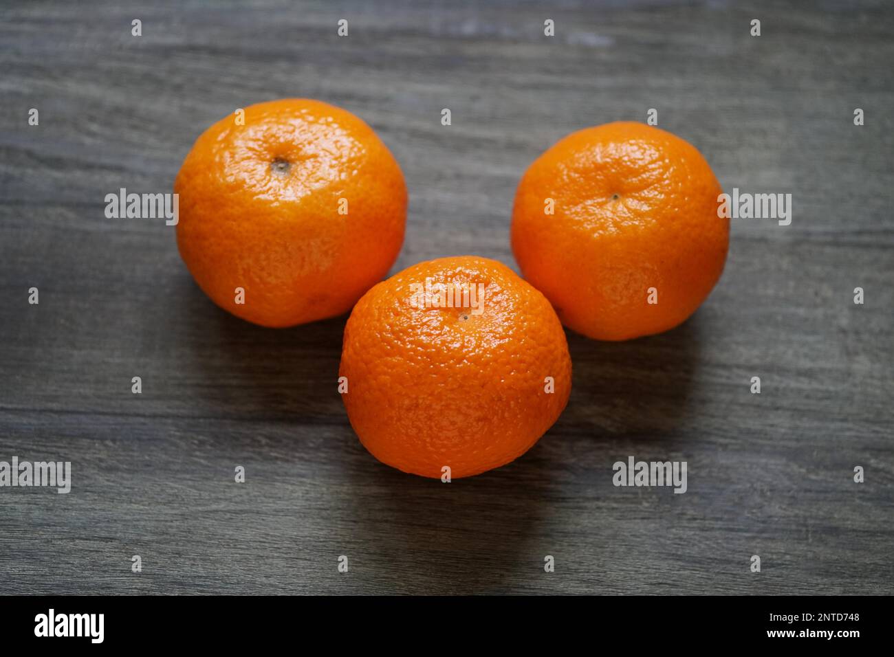 three whole clementines or mandarin oranges on rustic wooden table with shallow depth of field