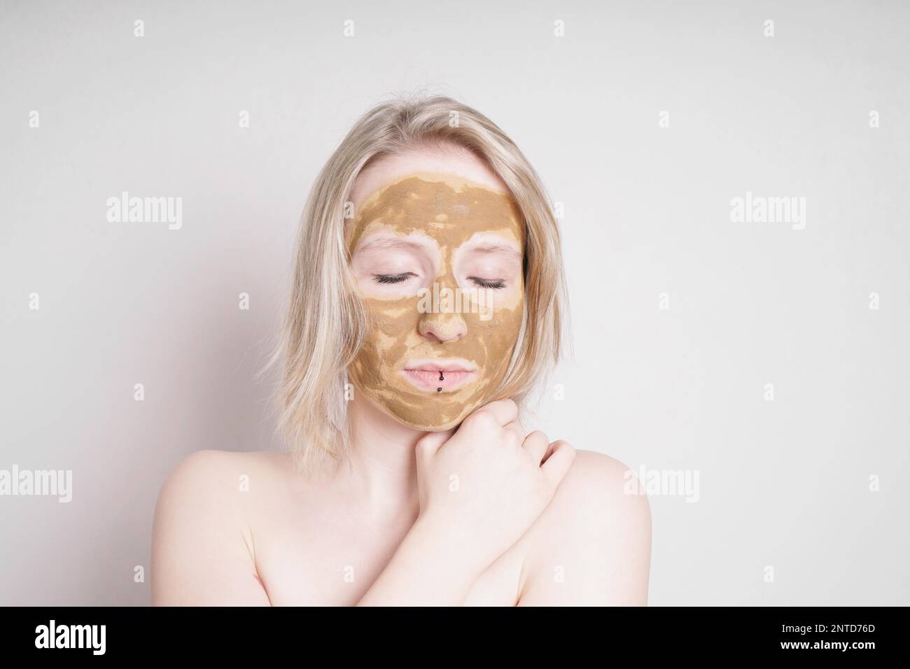 young woman with healing earth or clay beauty facial mask enjoying wellness treatment - a natural ayurveda treatment for acne or oily skin Stock Photo