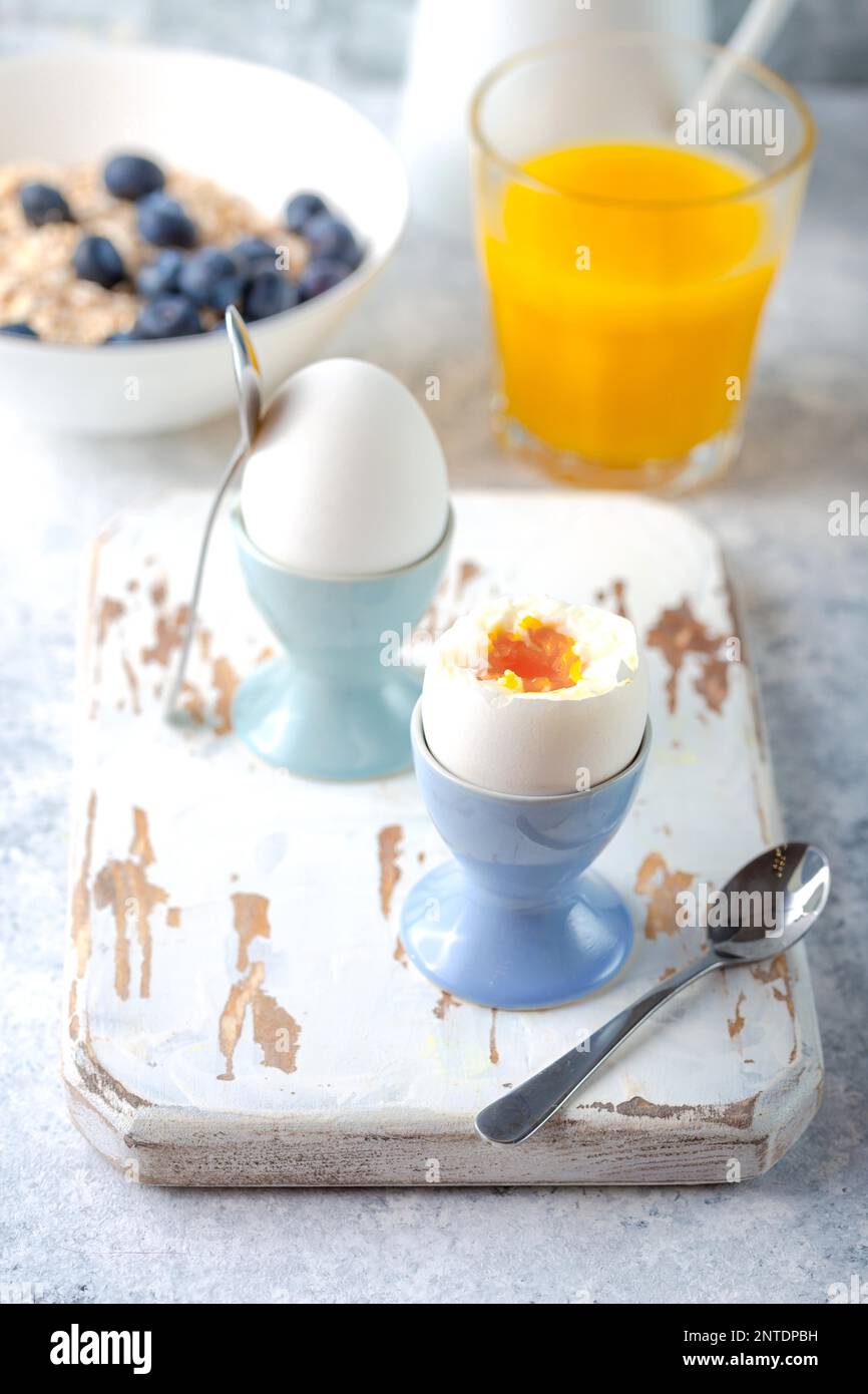 Fresh soft boiled eggs, oatmeal with blueberries, coffee, orange juice, milk. White concrete