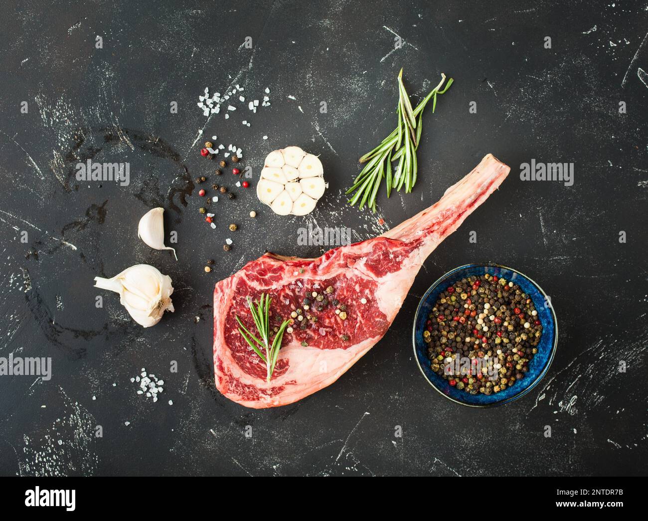 Raw marbled meat steak, herbs, seasonings, garlic, rustic stone background. Beef Rib eye steak on bone, ready for cooking. Top view. Ingredients for Stock Photo