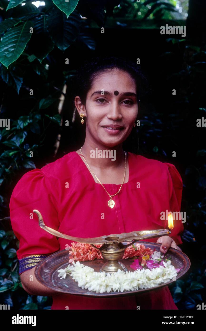 A girl holding oil lamp and flowers on a tray during Onam festival