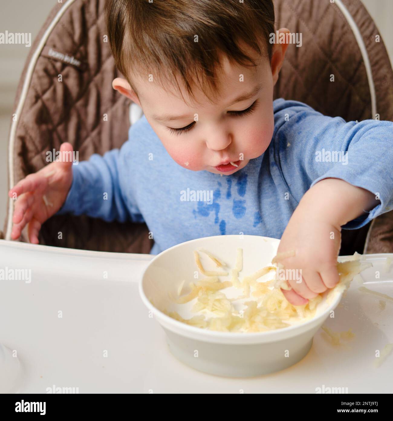 Funny child eating a grated apple with his hand from a plate, closeup