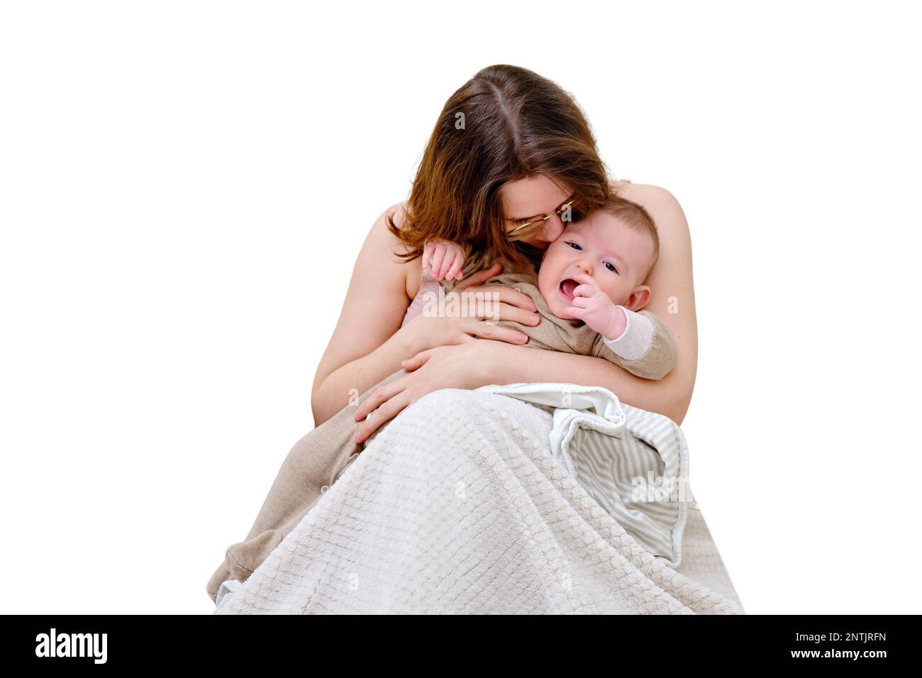 A mother woman kisses and comforts a crying infant baby boy sitting on the bed, isolated on a white background. Kid aged six months Stock Photo