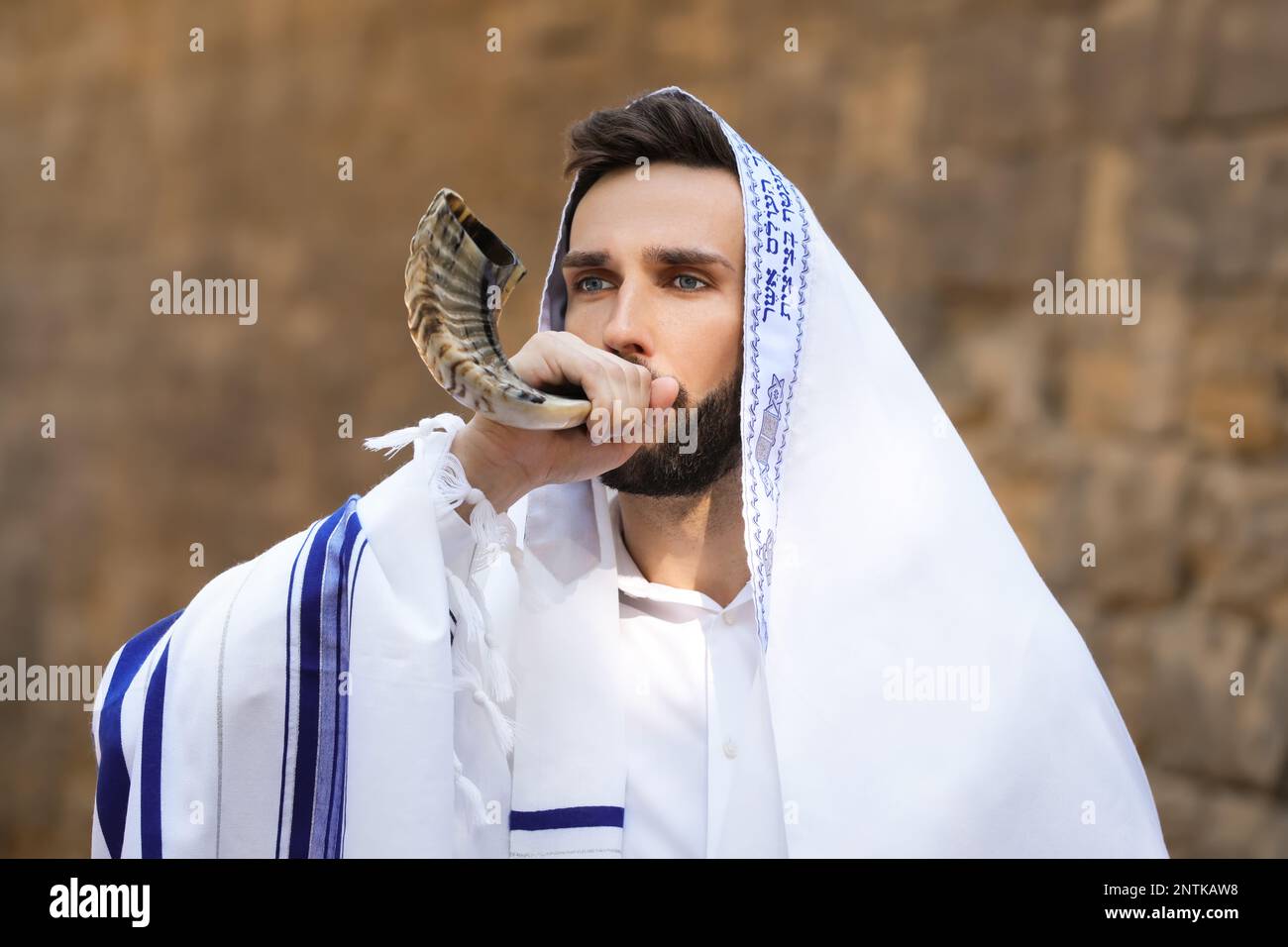 Jewish man blowing shofar on Rosh Hashanah outdoors. Wearing tallit