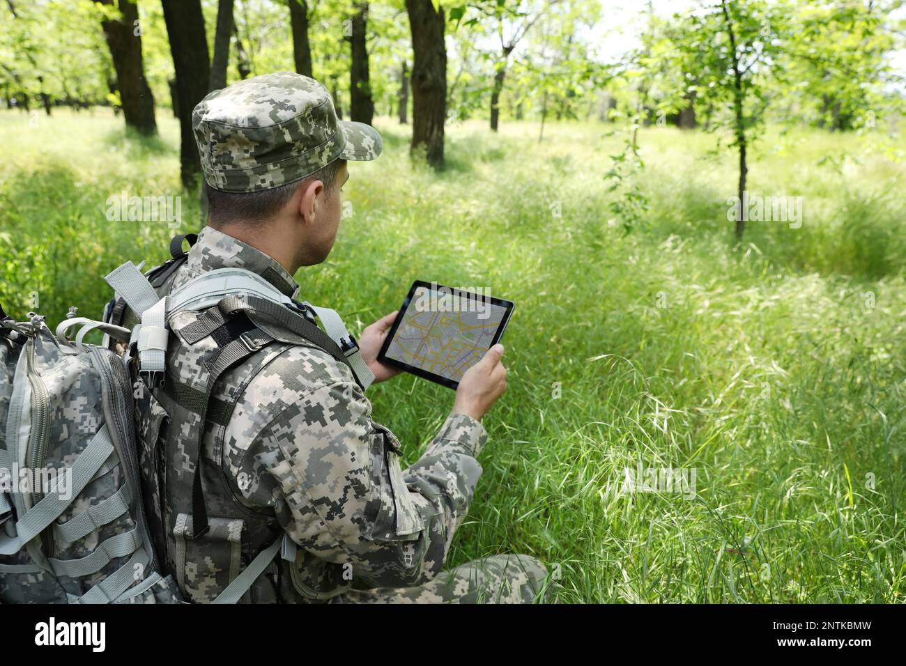 Soldier with backpack using tablet in forest Stock Photo