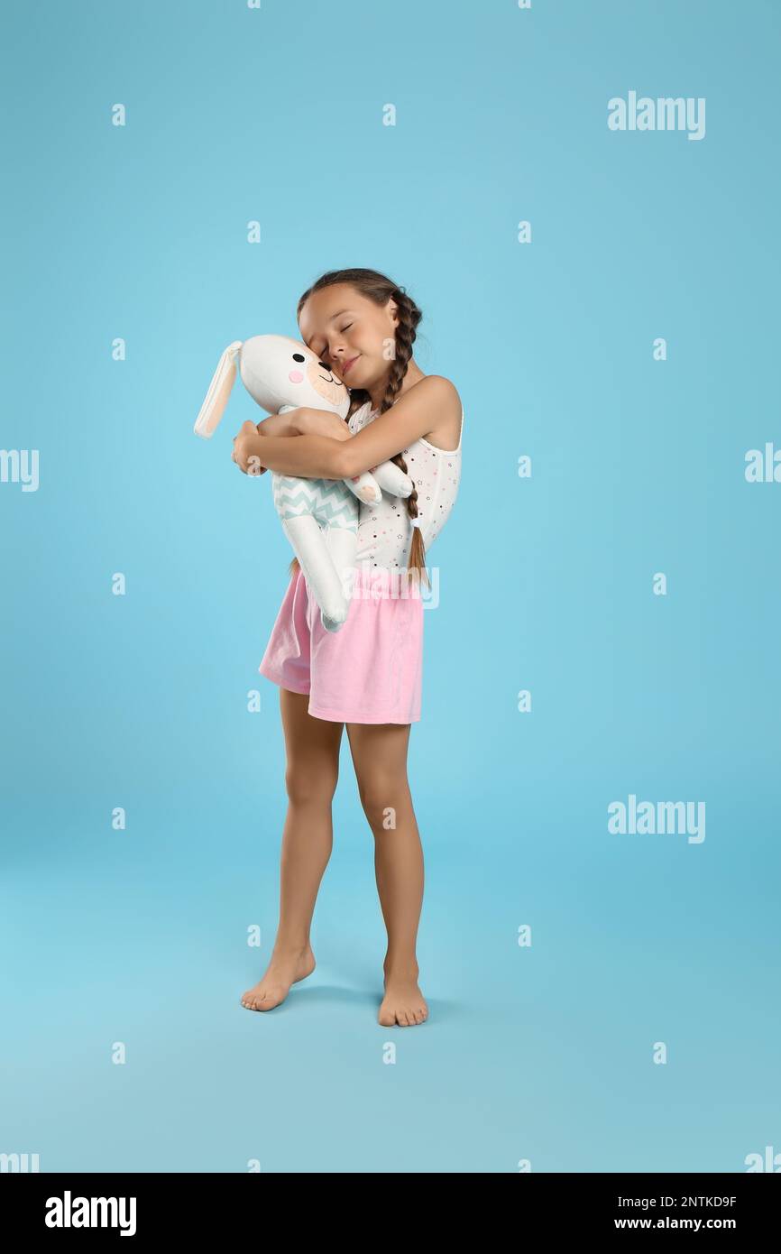 Cute girl wearing pajamas with toy on light blue background Stock Photo ...