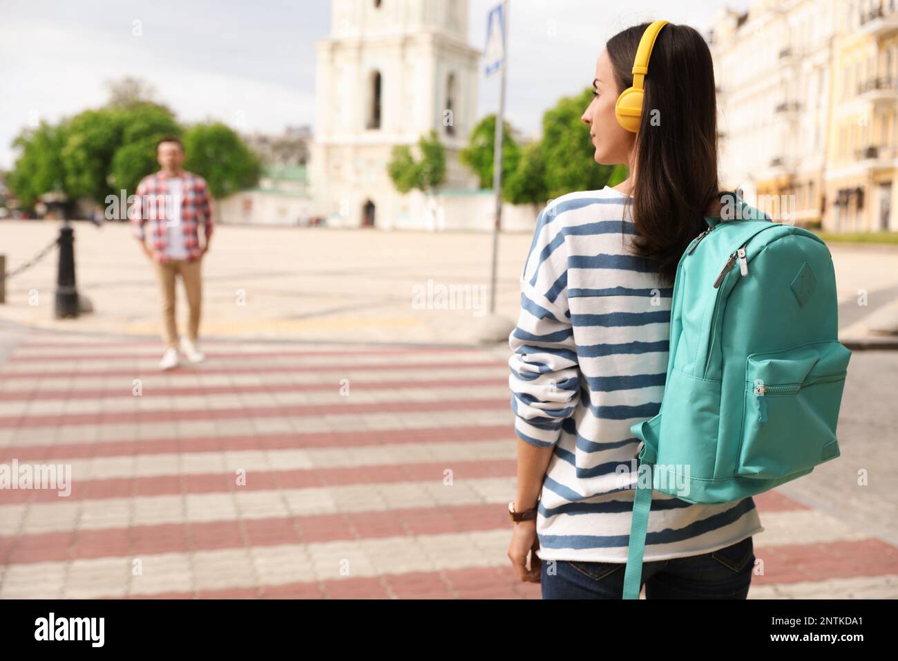 Young woman with headphones waiting to cross street. Traffic rules and