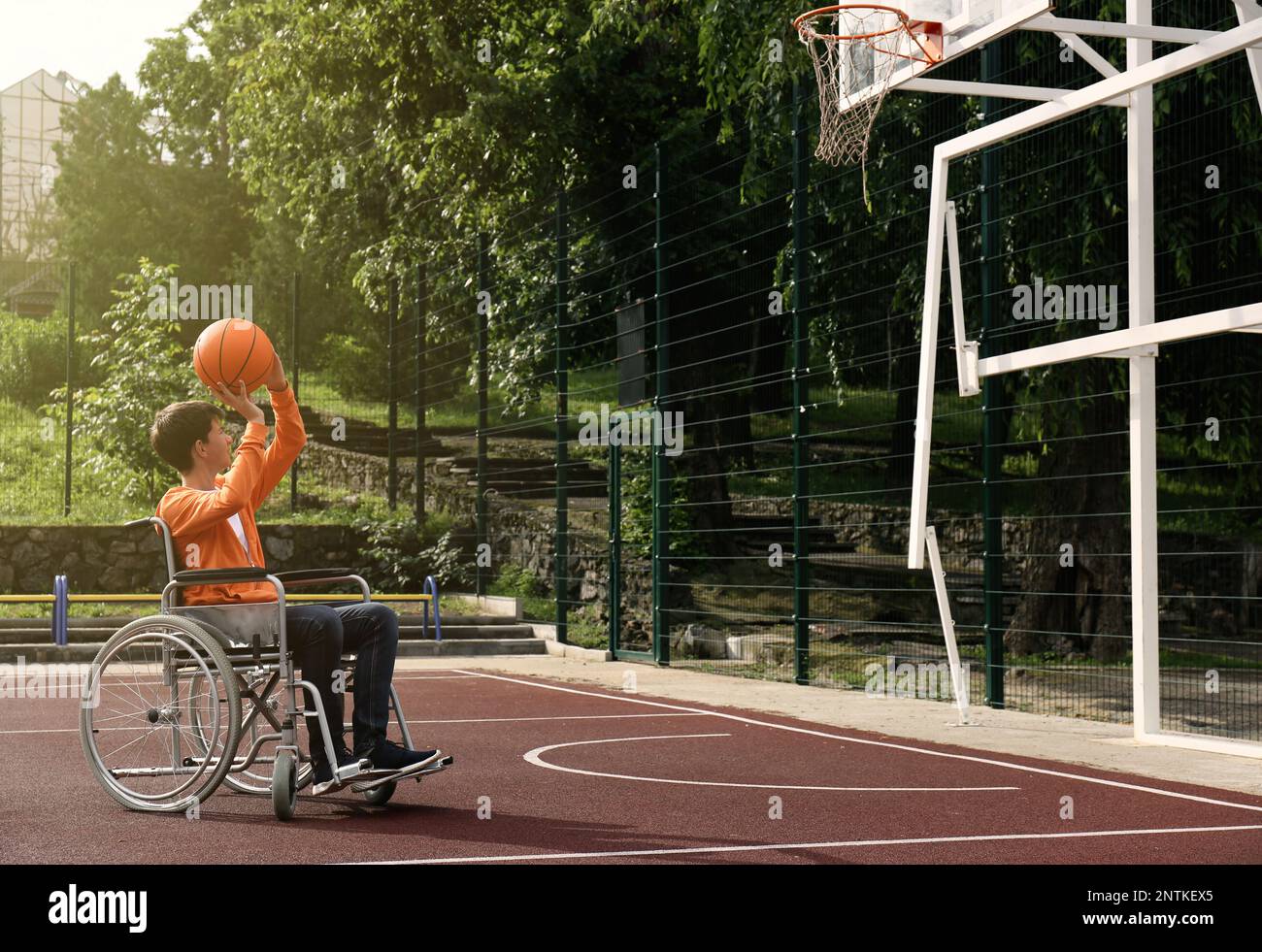 Disabled teenage boy in wheelchair playing basketball  on outdoor court Stock Photo