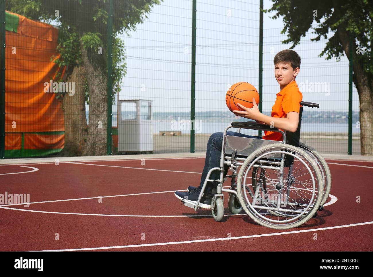 Disabled teenage boy in wheelchair with basketball ball at outdoor court Stock Photo