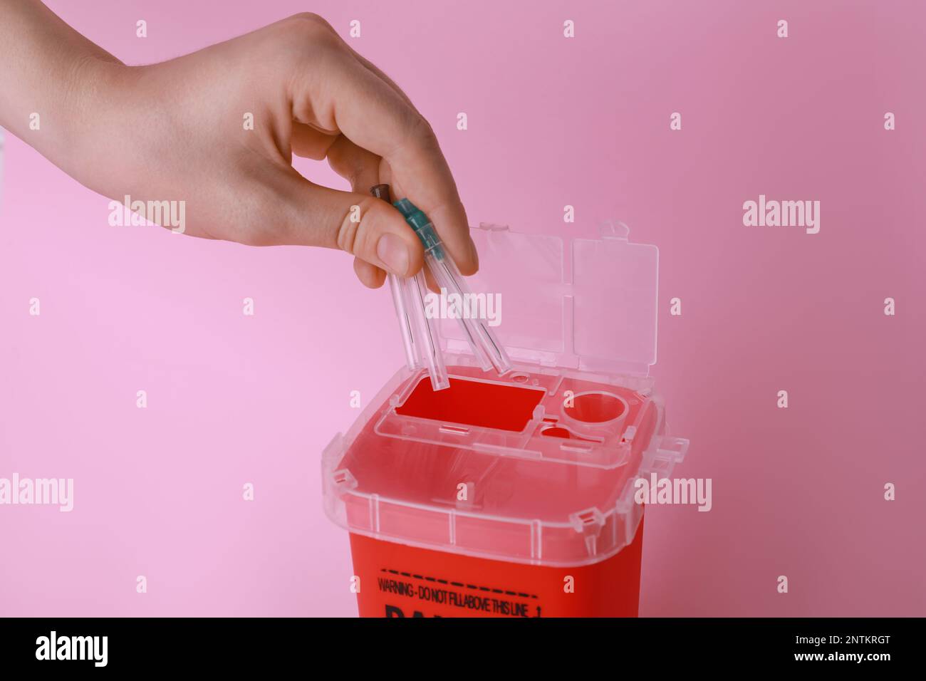 Woman throwing used syringe needles into sharps container on pink