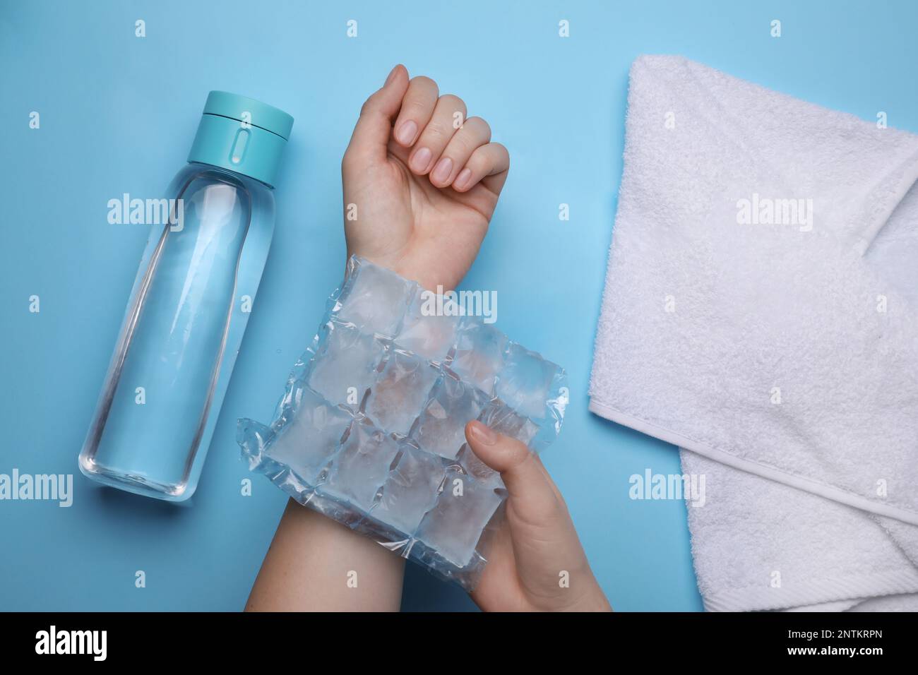 Woman with ice pack, bottle of water and towel on light blue background, top view. Heat stroke treatment Stock Photo