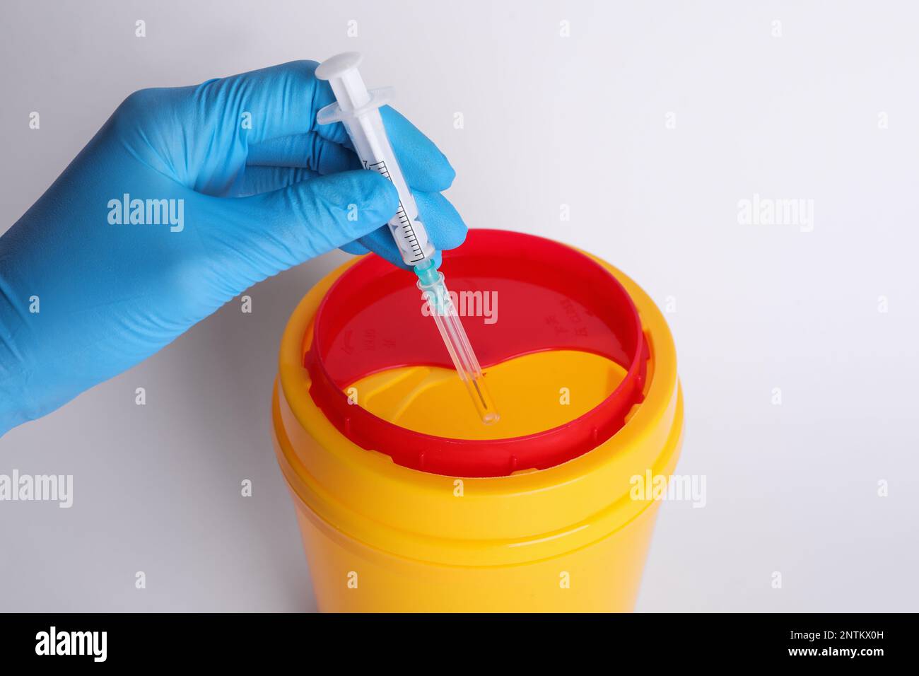 Doctor throwing used syringe into sharps container on white background, closeup Stock Photo