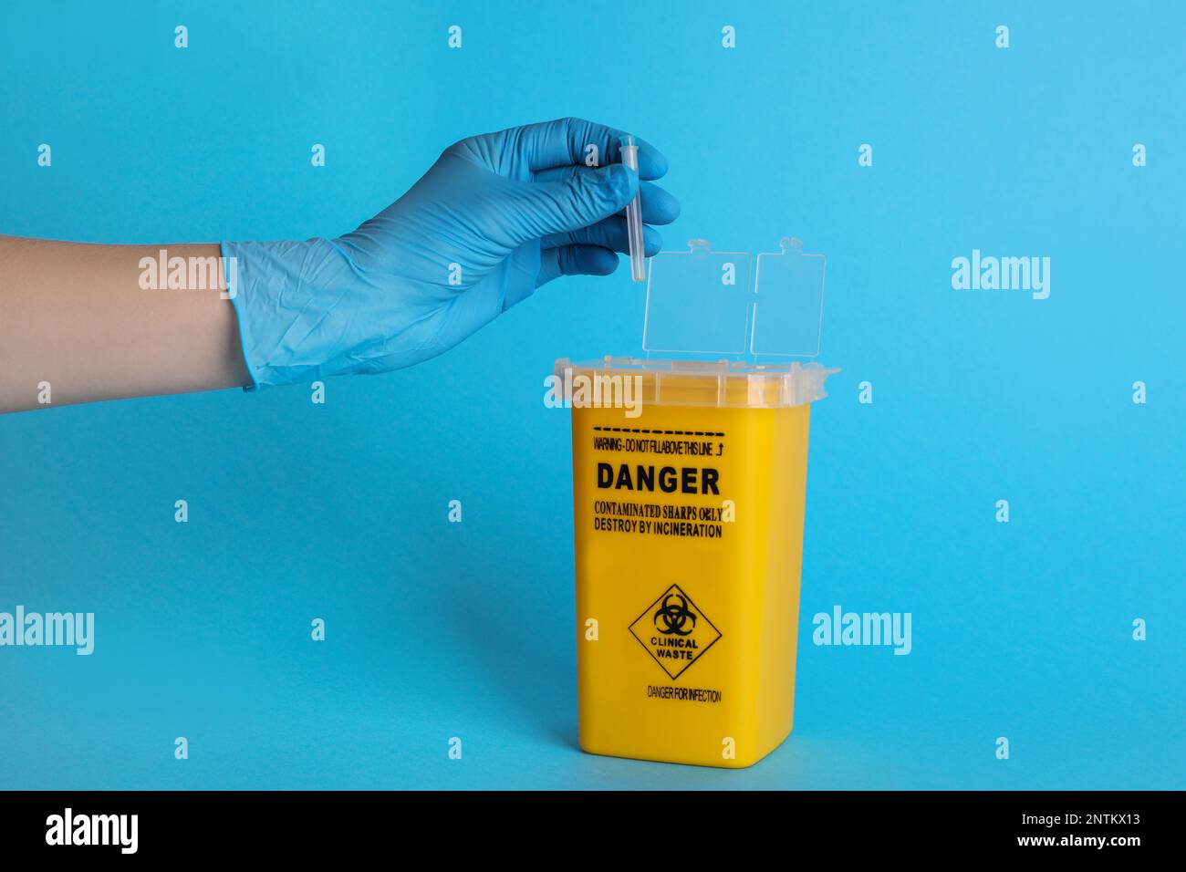 Doctor throwing used syringe needle into sharps container on light blue