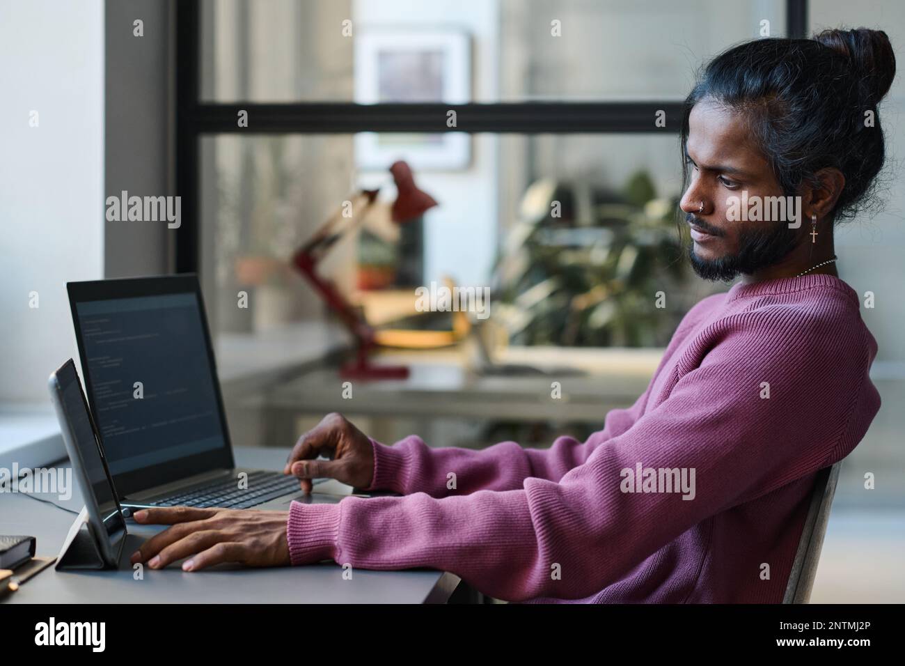 Young serious programmer working online with gadgets at his workplace, he typing codes for program Stock Photo