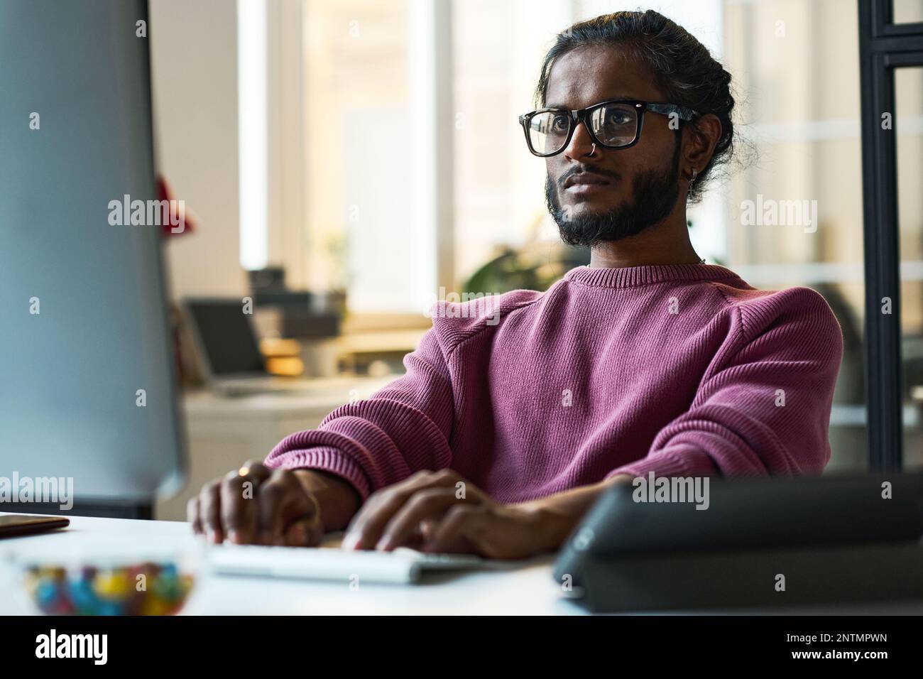 Serious young programmer in eyeglasses working online on computer at his workplace in IT office Stock Photo