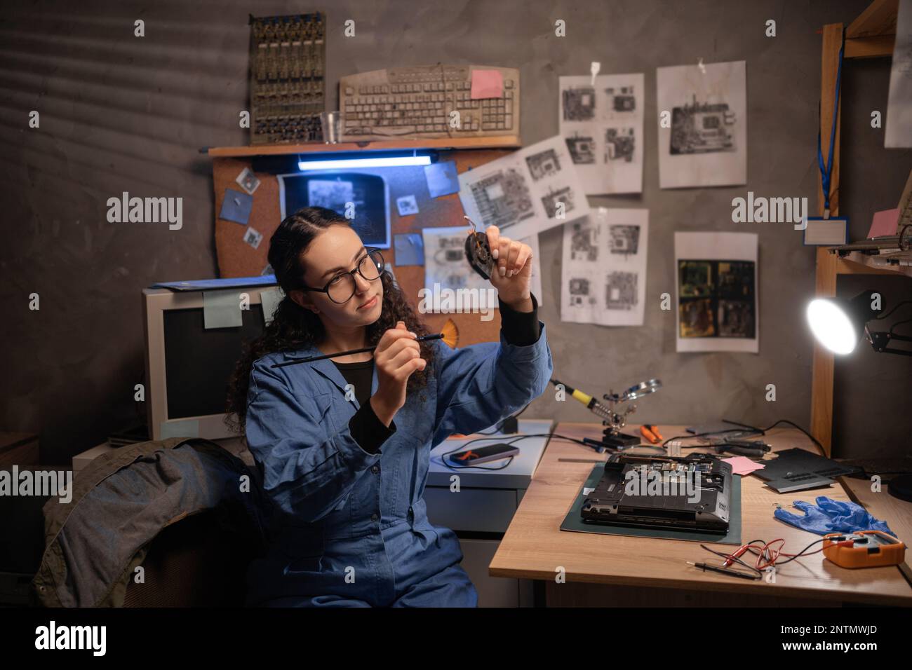 Female repairman disassembling laptop motherboard, holding a cooler fan