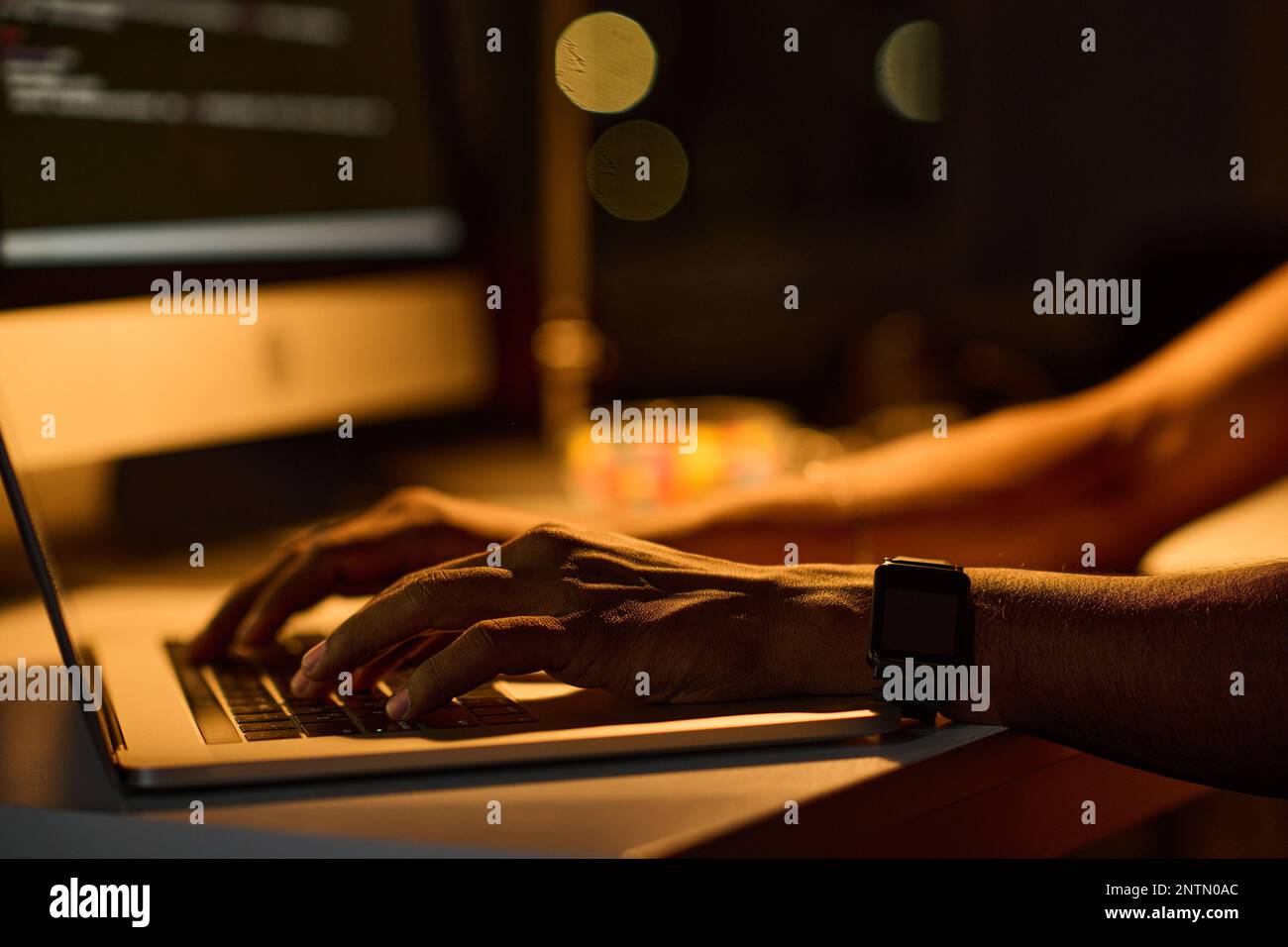 Close-up of young programmer sitting at table and typing codes on laptop working in dark office Stock Photo