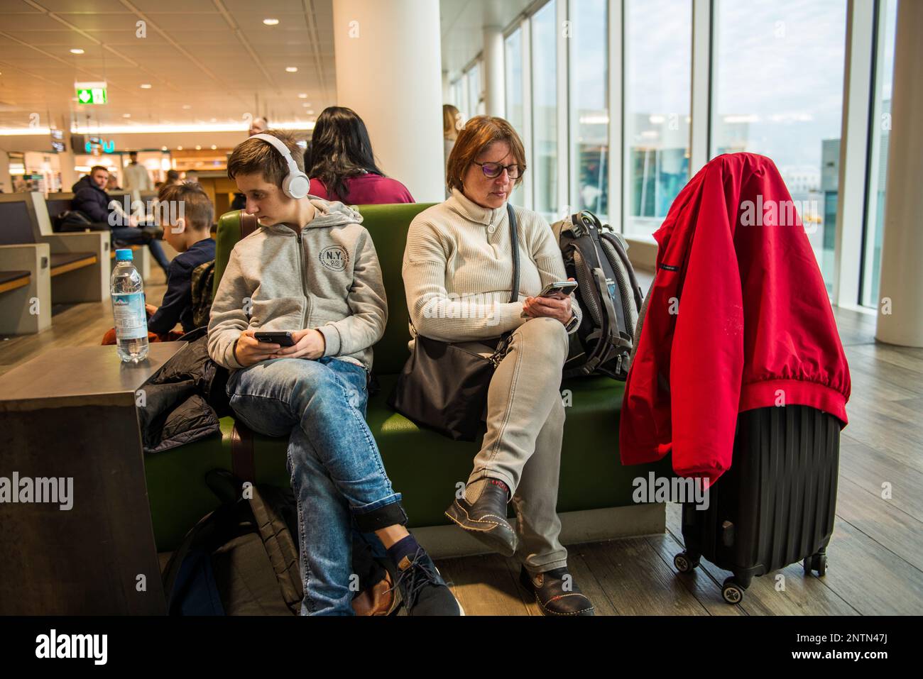 Munich,Germany- February 20,2023: Two people look at their smartphones while waiting for their flight to be announced. Stock Photo