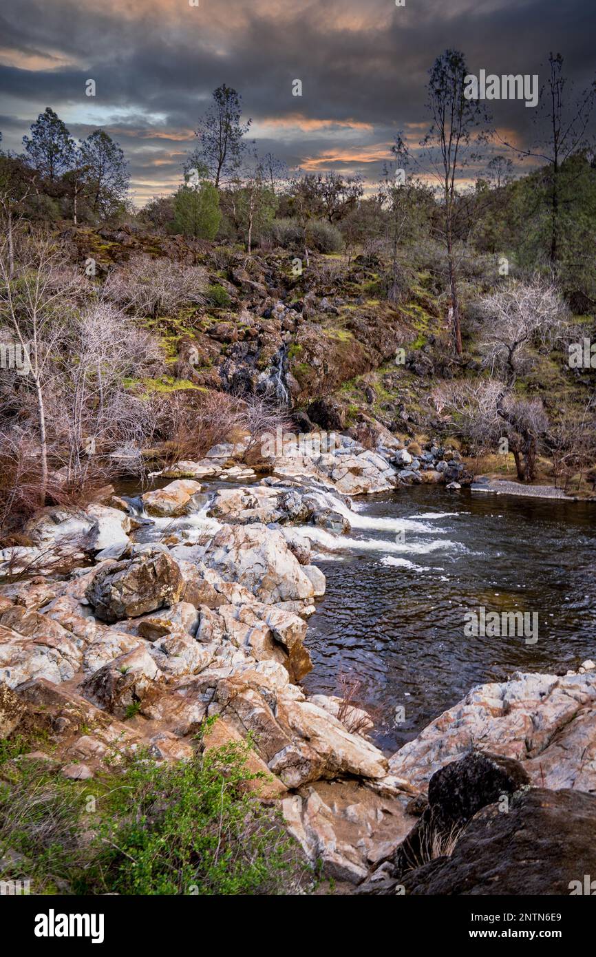 A vertical shot of a stream with long exposure surrounded by rocks and ...
