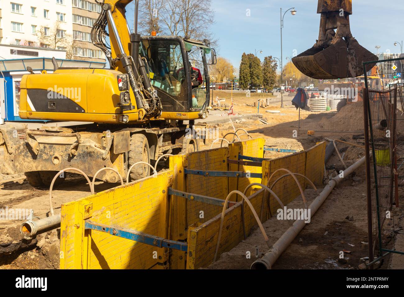 Excavator filling deep excavation supported by trench box with pipe