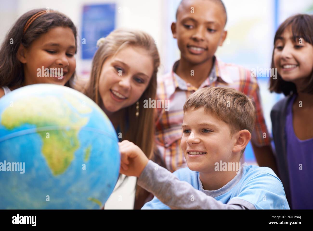 Here it is - Geography class. A group of pupils looking at a globe during geography class. Stock Photo