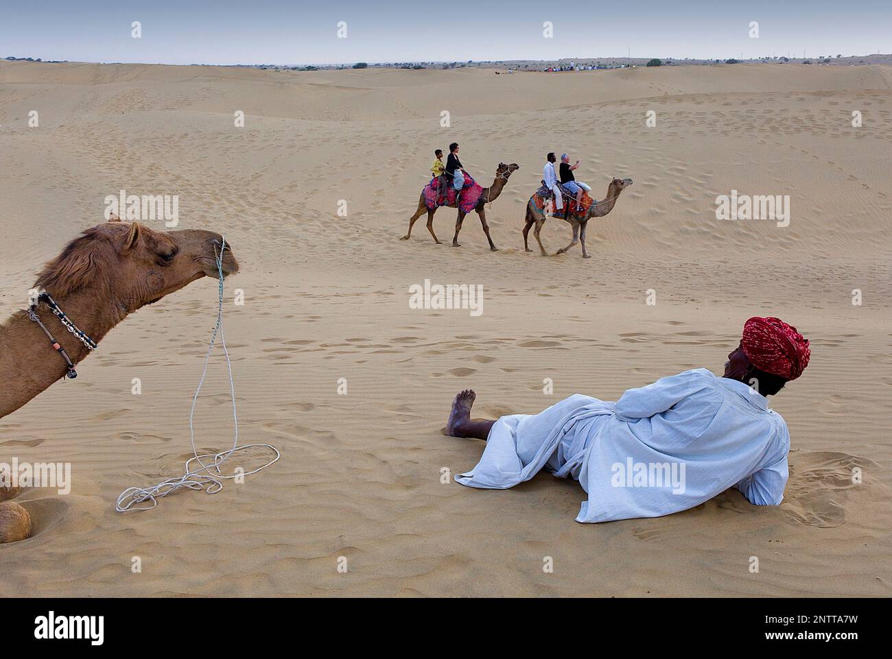 Native watching tourists riding camels on Sam dunes in Desert National ...