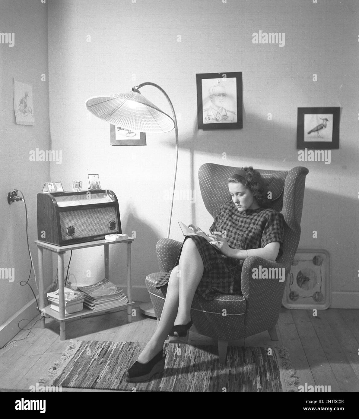 Radio listeners in the past. A woman is seen sitting in a armchair at home listening to the radio that sits on a small table in the room. On the front of the radio is a scale and when you turned the dial next to it so that the pointer was in the middle of a station name, that station was there. In addition to FM broadcasts, they also listened to foreign radio on longwave. Sweden in 1945 Kristofferson ref R13-3 Stock Photo